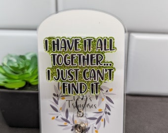 May include: A green glitter keychain with the text "I have it all together... I just can't find it". The keychain is on a white card with a wreath design and the text "Tillie's Treasures" and social media icons.