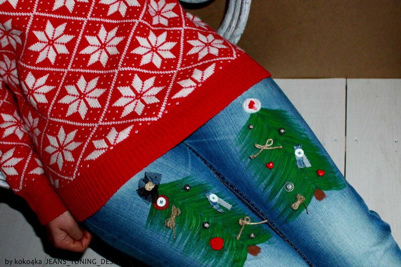 May include: A red and white sweater with a diamond and snowflake pattern paired with blue denim jeans featuring two hand-painted green Christmas trees decorated with small buttons, bows, and twine accents on the front of the legs.