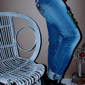 May include: Blue denim jeans featuring a reindeer graphic on the back pocket and a green painted design on the side. The jeans are paired with a red sweater with a white snowflake pattern and black leather boots. Text reads: koko4ka JEANS_TUNING_DESIGN.