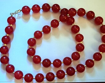 May include: A long red beaded necklace with gold spacers. The necklace is made of round beads and is strung on a gold chain.
