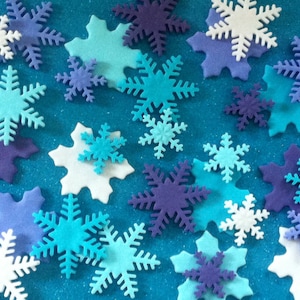 May include: Assortment of blue, white and purple snowflake-shaped decorations on a blue sparkly background.