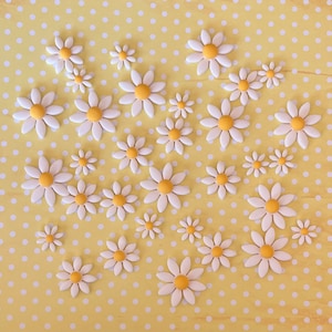 May include: A collection of white daisy-shaped decorations with yellow centres. The daisies are arranged in a heart shape on a yellow background with white polka dots.