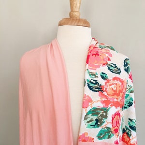 May include: A pink and white floral fabric with a pink solid fabric on the other side. The fabric is draped over a white mannequin.
