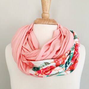 May include: A pink infinity scarf with a floral print on one side. The scarf is displayed on a white mannequin.