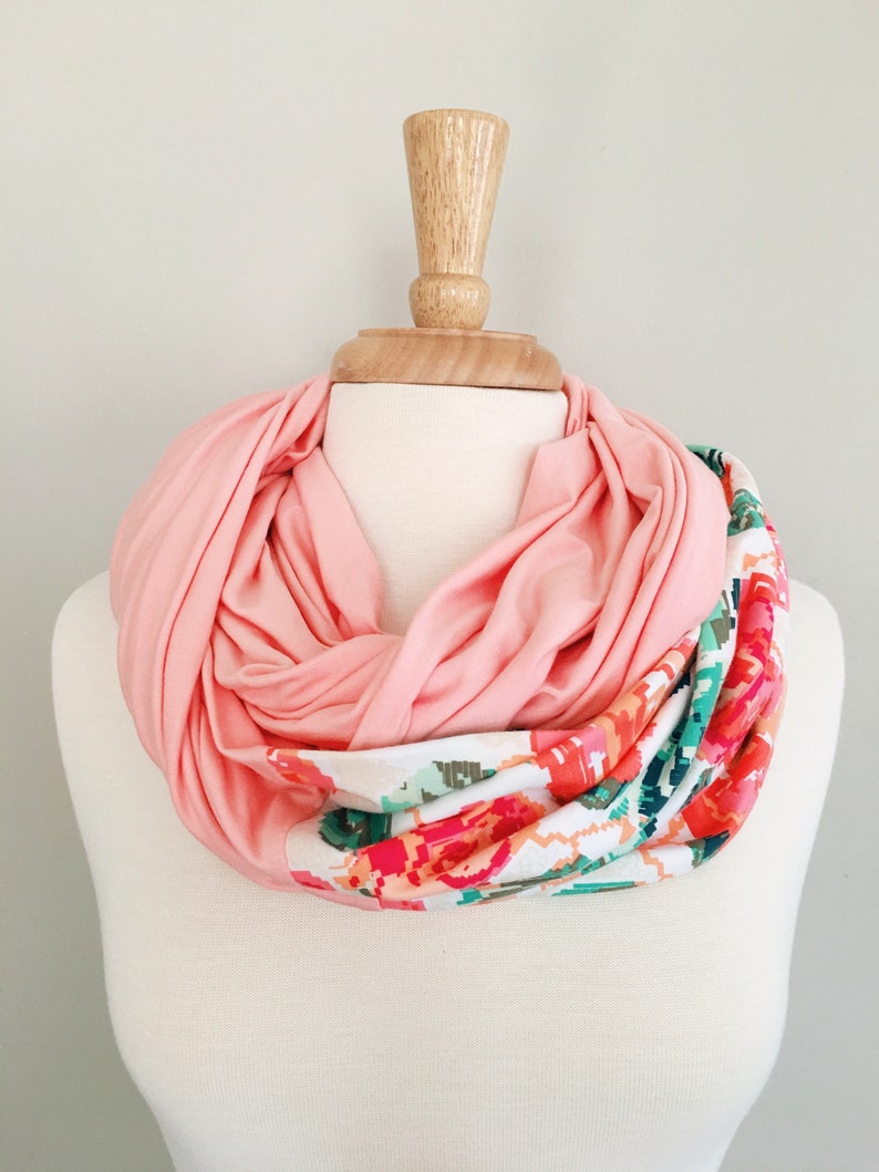 May include: A pink infinity scarf with a floral print on one side. The scarf is displayed on a white mannequin.