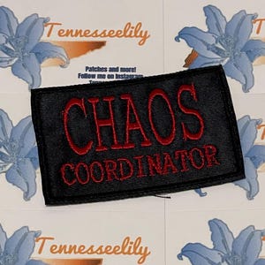 May include: A black embroidered patch with the words "CHAOS COORDINATOR" in red thread. The patch is rectangular and sits on a background of white cards with blue floral designs and the text "Tennesseelily".