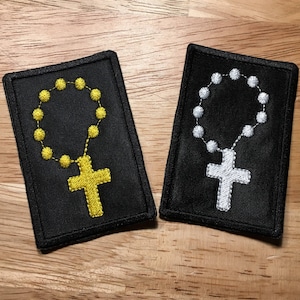 May include: Two black fabric patches with embroidered gold and silver rosaries and crosses.