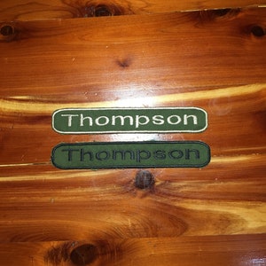 May include: Two green and black rectangular name tags with the name "Thompson" embroidered in white.
