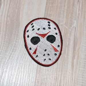 May include: White and red embroidered patch of a hockey mask with black eye holes.