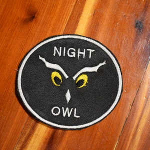 May include: A black and white embroidered patch with a white owl design and the words "NIGHT OWL" in white text.