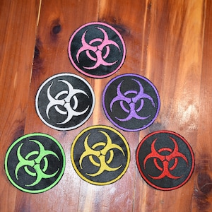 May include: Six embroidered biohazard symbol patches in different colors: pink, white, purple, green, yellow, and red. The patches are circular and have a black background.