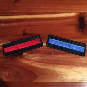 May include: Two thin rectangular patches, one red and one blue, with a black border. The patches are made of fabric and have a thin black line running through the center.