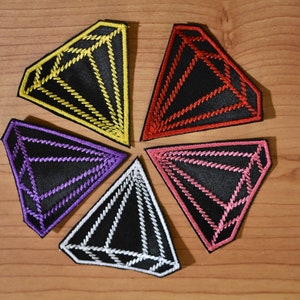 May include: Five diamond-shaped fabric patches in different colors. The patches are black with a diamond shape outlined in yellow, red, purple, pink, and white.