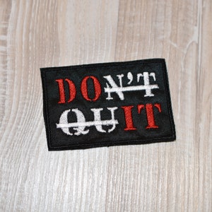 May include: Black embroidered patch with the words "DON'T QUIT" in red and white thread. The "T" in "DON'T" is crossed out with white thread.