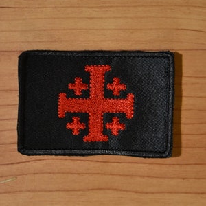 May include: A black patch with a red embroidered cross with four smaller crosses at each corner.