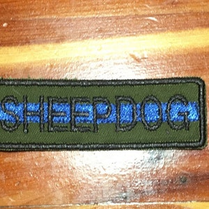 May include: A green and black embroidered patch with a blue stripe and the text "SHEEPDOG".
