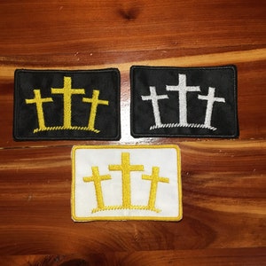 May include: Three embroidered patches with a design of three crosses. The crosses are yellow on a black background, white on a black background, and yellow on a white background.