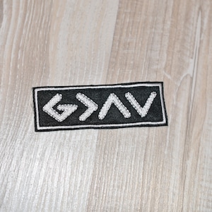 May include: Black and white embroidered patch with the word "GOD" written in a stylized font with arrows and a triangle.