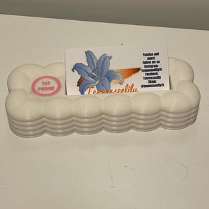 May include: A white, scalloped, rectangular business card holder with a pink circular 'TAP PHONE' icon. A white business card is inserted, featuring a blue lily graphic, an orange state silhouette, and text including 'Tenneeseelily' and social media handles.