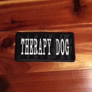 May include: Black patch with white text that reads "Therapy Dog".