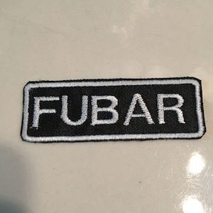 May include: A black and white embroidered patch with the word "FUBAR" in white lettering.