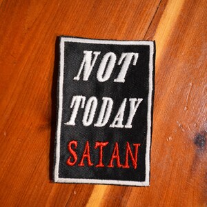 May include: Black patch with white embroidery that reads "NOT TODAY SATAN" with the word "SATAN" in red.