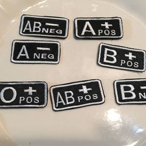 May include: Seven black and white embroidered patches with different blood types: AB-NEG, A+POS, A-NEG, B+POS, O+POS, AB+POS, B-NEG.