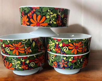 May include: Set of six vintage ceramic bowls with a floral pattern in shades of green, orange, yellow, and black. The bowls have a white base and are stacked on top of each other.