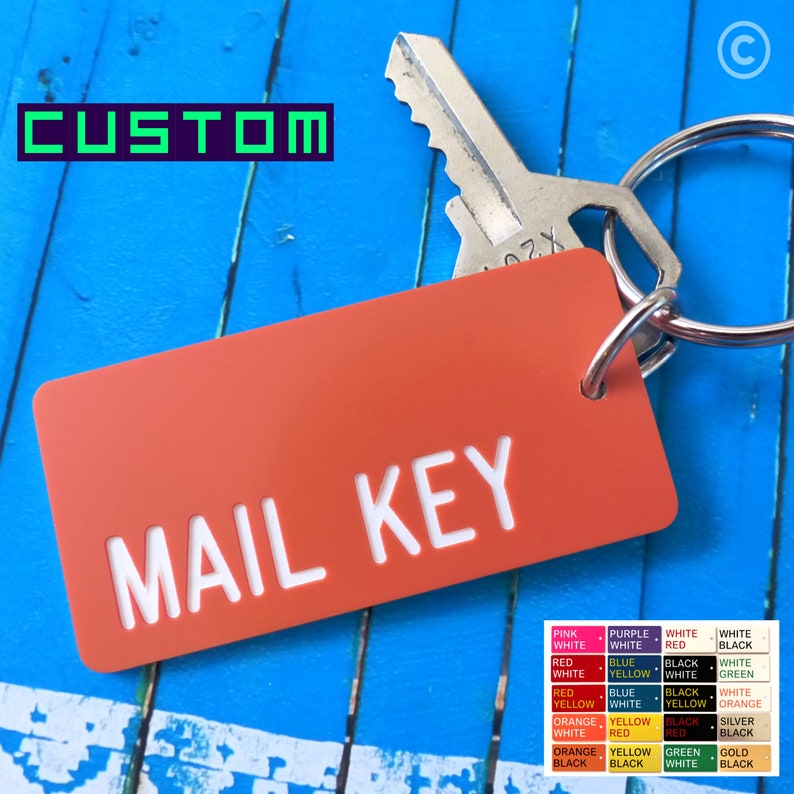 May include: A rectangular orange keychain tag with the white text MAIL KEY engraved on the front. The tag is attached to a silver metal keyring holding a single silver house key. A color chart is visible in the corner showing various options.