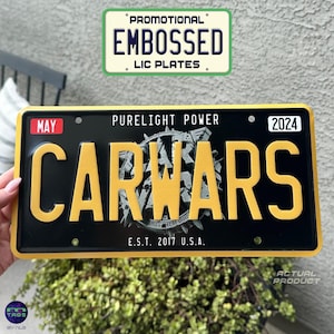 May include: Black and yellow metal license plate with the text "PURELIGHT POWER" and "CAR WARS" in large yellow letters. The plate also includes the text "MAY", "2024", and "E.S.T. 2017 U.S.A."