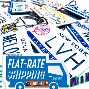 May include: A collection of rectangular white keychains featuring various sports team logos and names including Denver Broncos, UCLA Bruins, New York Yankees, and Los Angeles Dodgers. Each keychain has a metal ring attached at the top.
