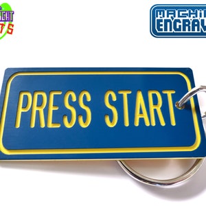 May include: Blue and yellow keychain with the text "PRESS START" in yellow letters. The keychain is machine engraved.
