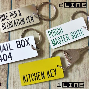 May include: Four rectangular metal keychains with split rings. One silver tag reads BIKE PEN & RECREATION PEN, one white tag reads PORCH MASTER SUITE, one white tag reads MAIL BOX 404, and one yellow tag reads KITCHEN KEY with a metal key attached.