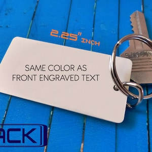 May include: A rectangular white keychain tag with rounded corners, attached to a silver metal split ring and a silver key. The tag features the text 'SAME COLOR AS FRONT ENGRAVED TEXT' and dimensions of 2.25 inches by 1.12 inches.