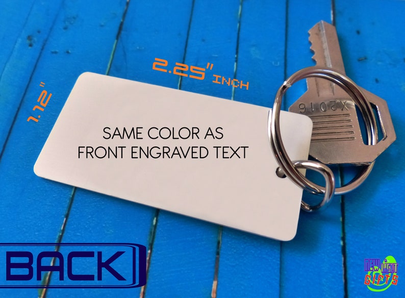 May include: A rectangular white keychain tag with rounded corners, attached to a silver metal split ring and a silver key. The tag features the text 'SAME COLOR AS FRONT ENGRAVED TEXT' and dimensions of 2.25 inches by 1.12 inches.