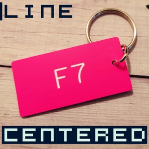 May include: A rectangular hot pink keychain tag featuring the white text F7 engraved in the center. The tag is attached to a circular silver metal split ring. The design is clean and simple, showcasing a vibrant color and clear lettering.
