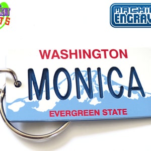 May include: A white license plate-shaped keychain with the name "MONICA" cut out in blue. The keychain features the text "WASHINGTON" and "EVERGREEN STATE" in red. A silver keyring is attached. The top left corner has the text "NEW LIGHT GIFTS".