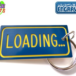 May include: A blue and yellow metal keychain with the text "LOADING..." on it. The keychain is attached to a silver key ring.