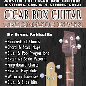 May include: A book cover titled "Cigar Box Guitar Technique Book" by Brent Robitaille. The cover features a close-up of a cigar box guitar and its neck. The book lists topics such as chords, scale maps, blues, and fingerboard charts.