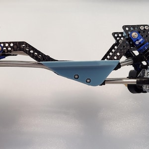 May include: A detailed view of a model car chassis, featuring a combination of black, blue, and silver components. The chassis includes suspension, shocks, and a central blue plate. The design suggests a focus on precision and performance.