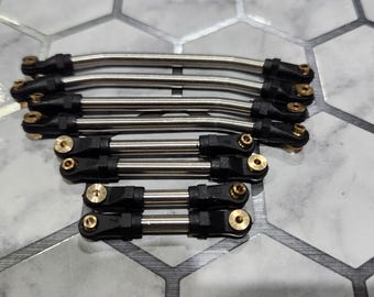 Pode incluir: Uma variedade de hastes de metal prateadas com conectores pretos e dourados. As hastes são curvas e retas, e estão dispostas em uma pilha organizada. Os conectores parecem ser feitos de plástico e latão. Estes são provavelmente componentes para um dispositivo mecânico.