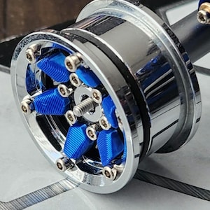 Puede incluir: Primer plano de una brillante rueda cromada con detalles azules. La rueda presenta una llanta plateada pulida, radios azules y pernos plateados. La rueda está diseñada para un vehículo y se encuentra sobre un fondo neutro.