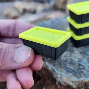 Pode incluir: Um conjunto de quatro recipientes de armazenamento de plástico preto com tampas amarelo brilhante. Os recipientes estão empilhados uns sobre os outros.