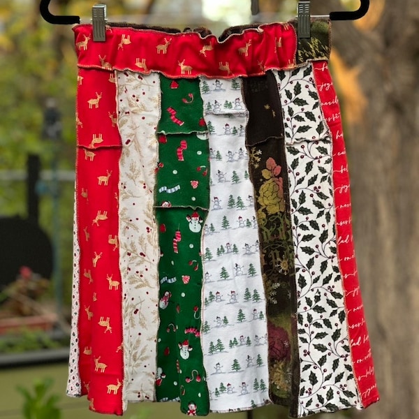 Könnte beinhalten: Ein Patchwork-Rock aus verschiedenen Stoffen mit Weihnachtsmotiven. Der Rock ist rot, grün, weiß und braun mit verschiedenen Mustern, darunter Rentiere, Schneemänner und Stechpalmen.