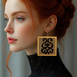 May include: A woman with red hair styled in a braid and bun, wearing large square gold earrings. The earrings have a black patterned design. She is wearing a black lace turtleneck.