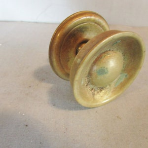 May include: A vintage brass door knob with a tarnished finish. The knob features a rounded center and two oval-shaped plates. The brass has a greenish patina in some areas, indicating age and use. This hardware is suitable for antique or vintage home decor.