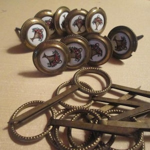 May include: A set of 10 brass cabinet knobs with a floral design. The knobs are round and have a white porcelain insert with a red and green floral design. The knobs are attached to a brass screw.