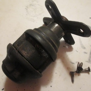 May include: A dark, matte black metal furniture caster featuring a rounded, bulbous wheel housing and a three-pronged mounting plate with pre-drilled holes. Three small, silver-toned metal screws are positioned separately near the caster.