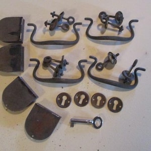 May include: A collection of antique hardware pieces, including door handles, keyhole covers, and a key. The pieces are made of metal and have a rustic, aged look.