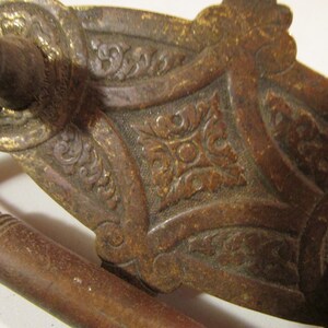 May include: Close-up of a vintage wooden sword hilt and handle. The hilt features ornate, carved floral designs with gold accents. The handle is a dark brown color with carved rings.